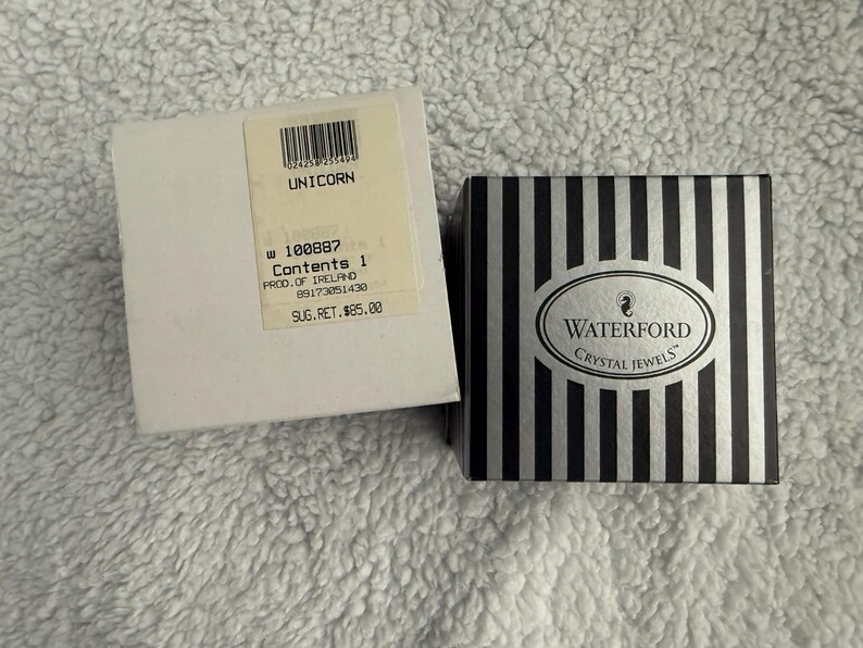 May include: A white box with black text that reads "UNICORN 100887 Contents 1 PROD. OF IRELAND 09173051430 SUG.RET. $85.00" and a black and white striped box with the text "WATERFORD CRYSTAL JEWELS".