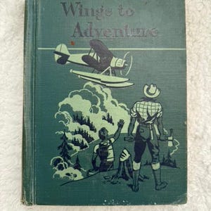 May include: A vintage green hardcover book titled "Wings to Adventure" with an illustration of a plane flying over a mountain range and two people standing in the foreground.