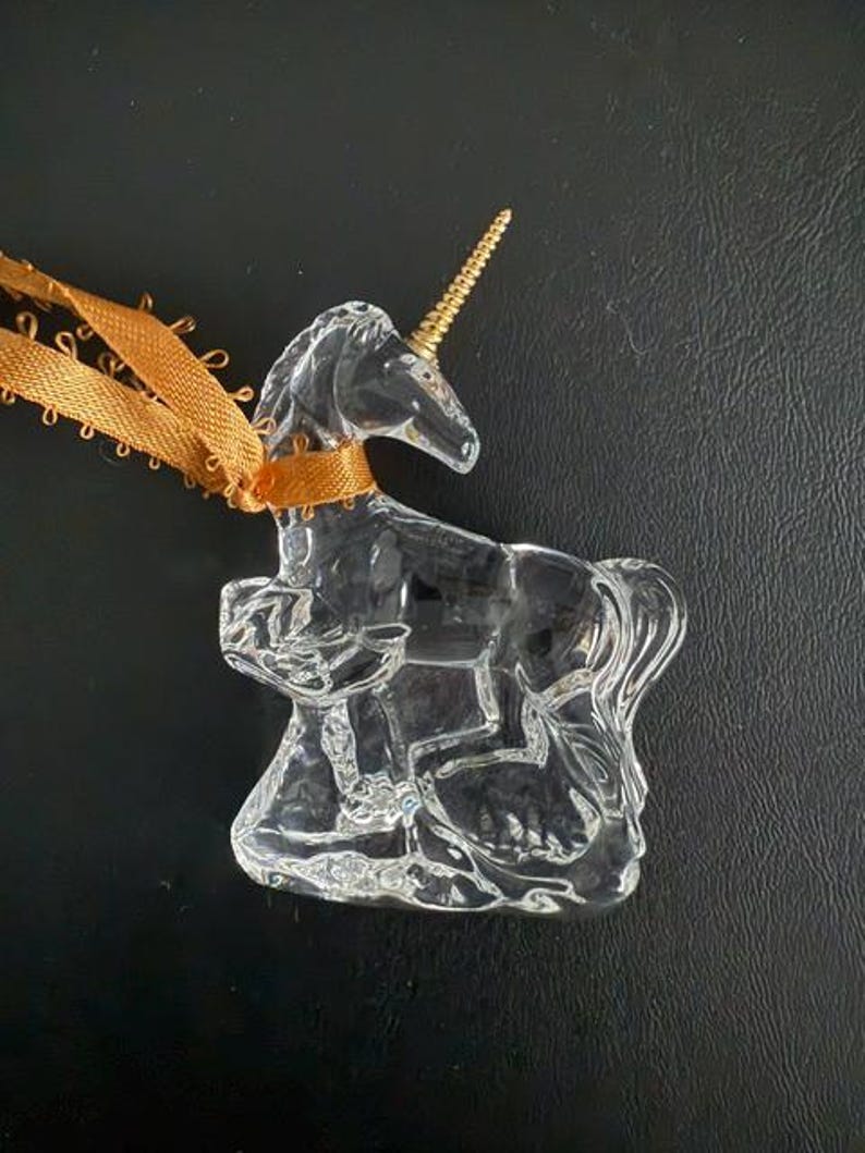May include: A clear glass unicorn ornament with a gold horn. The ornament is hanging from a brown ribbon.