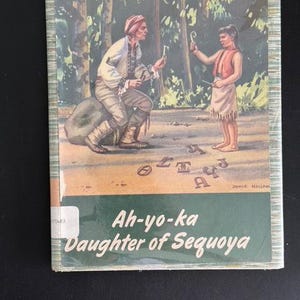 May include: A book cover with a green background and a picture of two people in a forest. The title of the book is "Ah-yo-ka Daughter of Sequoya".