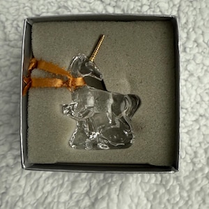 May include: A clear glass unicorn figurine with a gold horn, sitting in a grey box with a gold ribbon.