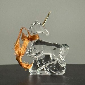 May include: A clear glass unicorn figurine with a gold horn and a brown ribbon tied around its neck.