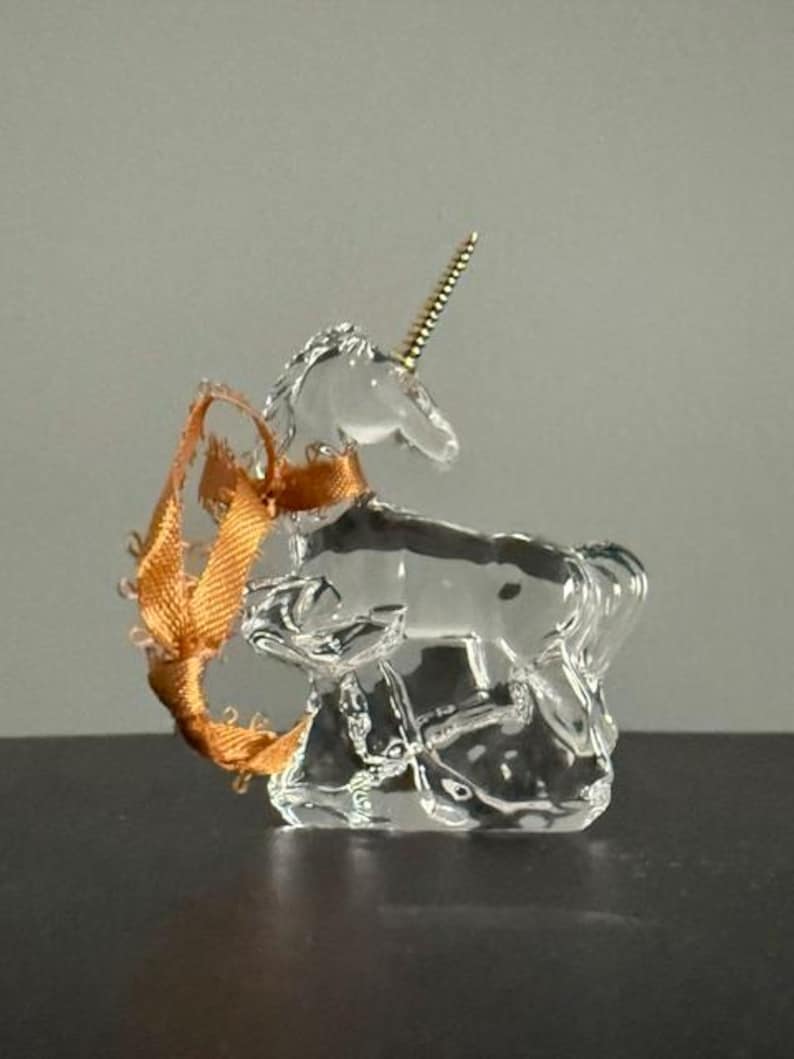 May include: A clear glass unicorn figurine with a gold horn and a brown ribbon tied around its neck.