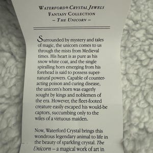 May include: A white card with black text describing the Waterford Crystal Fantasy Collection - The Unicorn. The text describes the unicorn as a mythical creature with magical powers and a symbol of purity. The card is surrounded by a white fuzzy background.