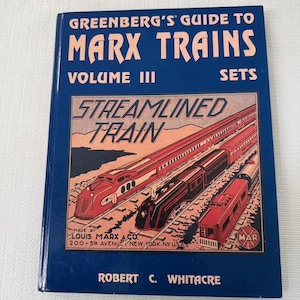 May include: A blue book titled "Greenberg's Guide to Marx Trains, Volume III, Sets." The cover features illustrations of red and black streamlined trains. The book is published by Louis Marx & Co. of New York, USA.