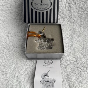 May include: A Waterford Crystal Jewels Fantasy Collection The Unicorn ornament. The unicorn is made of clear crystal and has a gold horn. The ornament comes in a white box with a black and white striped lid.