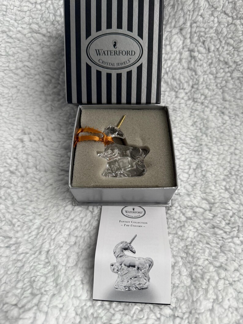 May include: A Waterford Crystal Jewels Fantasy Collection The Unicorn ornament. The unicorn is made of clear crystal and has a gold horn. The ornament comes in a white box with a black and white striped lid.