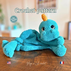 Peut inclure: Une peluche crochetée bleu sarcelle avec une petite corne orange sur la tête et de grands yeux sombres. Le texte "Crochet pattern" et "PDF PATTERN ONLY" est visible. La peluche a une finition en fil texturé doux et des membres noués.