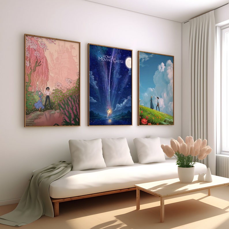 May include: Three framed movie posters with a white couch and a coffee table in front of them. The posters are of the movie "Howl's Moving Castle". The first poster shows a pink and green landscape with a young woman and a man walking in the distance. The second poster shows a blue sky with a shooting star and a moon. The third poster shows a green field with a young woman and a man walking in the distance.
