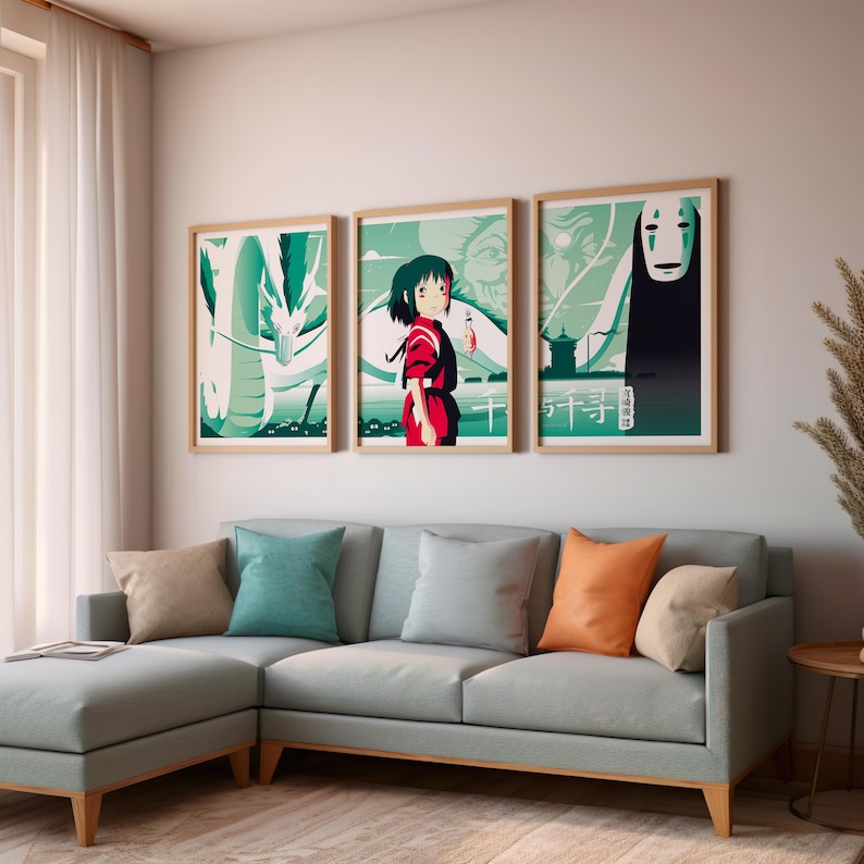 May include: Three framed posters with a green and white background featuring characters from the animated film Spirited Away. The posters are hung on a white wall above a light blue sectional sofa with pillows.