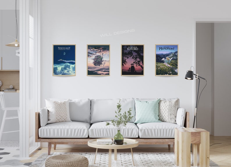 May include: Four framed movie posters with gold frames are displayed on a white wall. The posters feature artwork from animated films, including "Spirited Away," "Castle in the Sky," "My Neighbor Totoro," and "Princess Mononoke." A white sofa with pillows sits below the posters.
