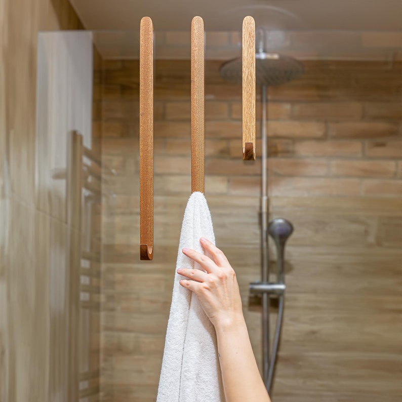 Hand placing a towel onto a wooden hook attached to a shower cabin glass. Easy and comfortable.