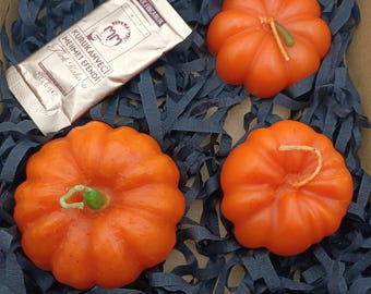 Könnte beinhalten: Drei orangefarbene Kerzen in Kürbisform in einer Geschenkbox mit schwarzem Schredderpapier. Die Box enthält außerdem ein kleines Päckchen türkischen Kaffees mit der Aufschrift "KURUKAHVECI MEHMET EFENDI Turk Kahvesi NET 100 GR".