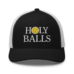 May include: Black and white trucker hat with a black brim and a white mesh back. The hat has a yellow and white embroidered pickleball and the text "HOLY BALLS" in white.