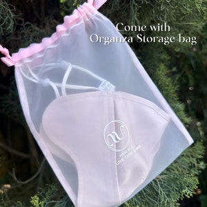 May include: A white silk face mask with the text "M&W SILK LOVE CARE SHINE" and a white letter "M" logo. The mask is in a white organza storage bag with a pink drawstring.