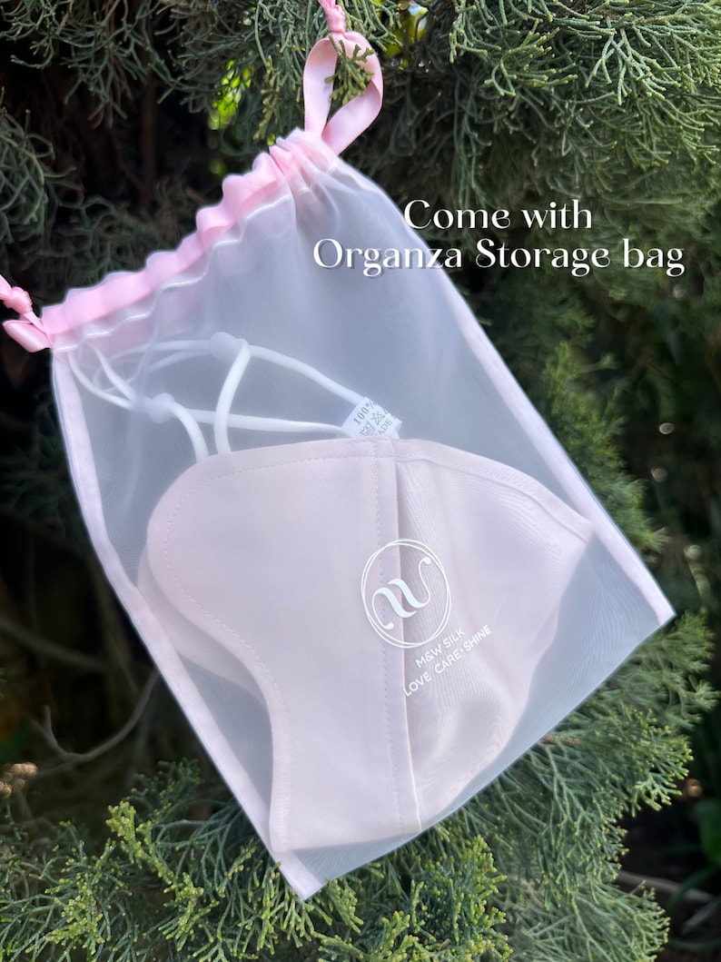 May include: A white silk face mask with the text "M&W SILK LOVE CARE SHINE" and a white letter "M" logo. The mask is in a white organza storage bag with a pink drawstring.
