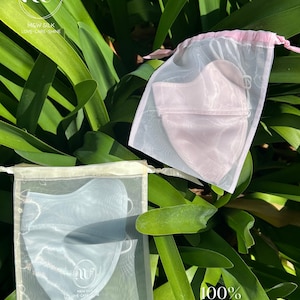 May include: Two silk face masks in separate white mesh bags. The mask on the left is light blue and the mask on the right is light pink. Both bags have a white logo with the text "M&W SILK LOVE CARE SHINE". The text "100% Mulberry Silk" is written below the bags.
