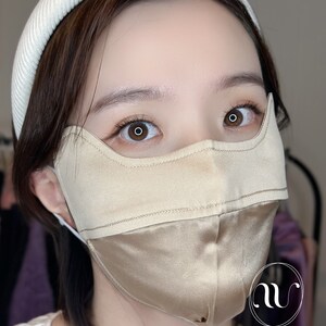 May include: A person wearing a light brown silk face mask with a white headband. The mask has a seam down the center and the text "M&W SILK LOVE.CARE.SHINE" is printed on the bottom right corner.