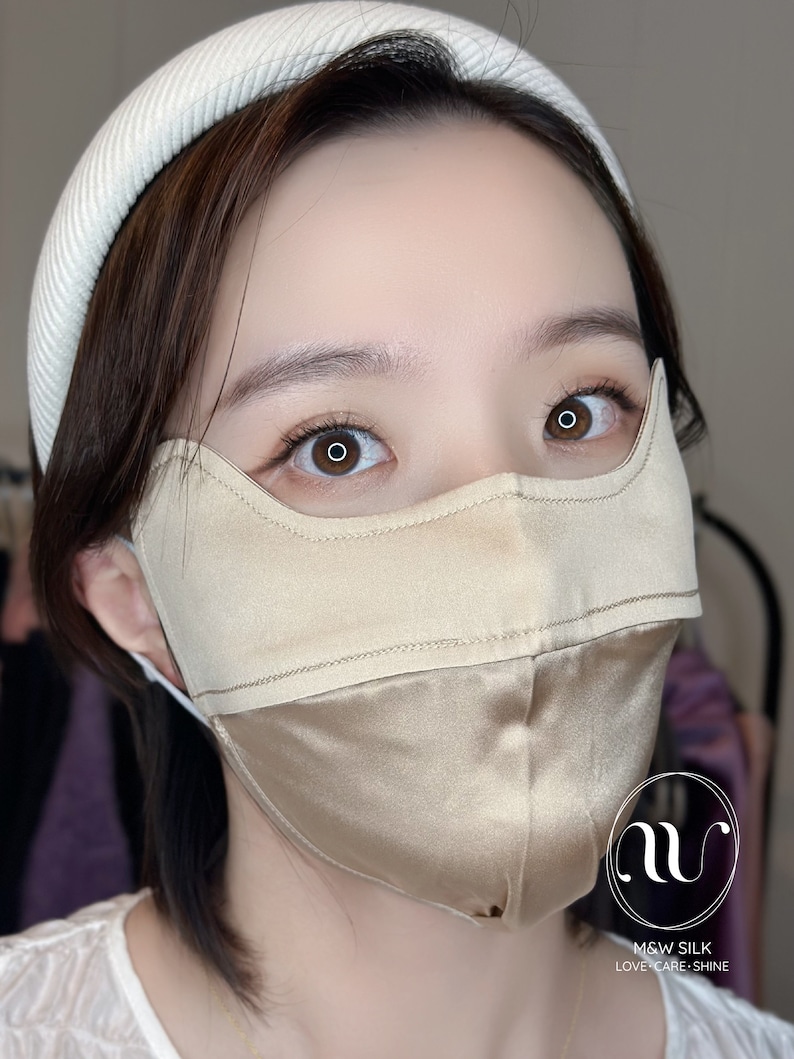 May include: A person wearing a light brown silk face mask with a white headband. The mask has a seam down the center and the text "M&W SILK LOVE.CARE.SHINE" is printed on the bottom right corner.
