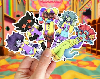 May include: Five colorful cartoon character stickers with different expressions. The stickers are on a hand and feature a black and purple character, a purple and yellow character, a yellow and green character, a red and blue character, and a multi-colored character. The stickers are all on a colorful background with the text "Jovial Playground".
