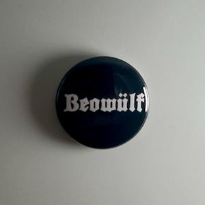 May include: A black button with the word "Beowulf" in white lettering.