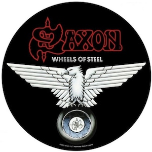 May include: A black and white circular sticker with a red "Saxon" logo and the words "Wheels of Steel". A white eagle with outstretched wings is centered on the sticker, with a black and white tire in the background.