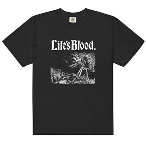 May include: A black short-sleeve t-shirt featuring a white graphic print on the chest. The design includes the text "Life's Blood." above a detailed black and white illustration of a figure amidst flames and clouds with rays of light.
