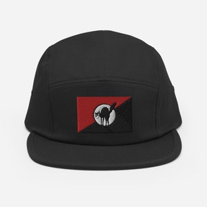 Puede incluir: Gorra negra de 5 paneles con una bandera roja y negra con una silueta blanca de un gato. La bandera está bordada en la parte delantera de la gorra.