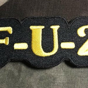 Puede incluir: Parche de tela negro con el texto "F-U-2" en letras bordadas amarillas.
