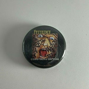 May include: A black and white button with a graphic of a face surrounded by ants. The text "PESTILENCE" and "CONSUMING IMPULSE" is printed on the button.