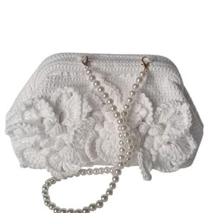 May include: A white crocheted clutch with a pearl beaded strap. The clutch features a floral design on the front and gold-colored clasps. The pearl strap is approximately 20 inches long.