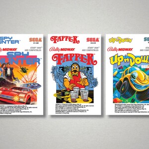 Pu&ograve; includere: Tre scatole di videogiochi vintage per console Atari 2600. Le scatole presentano grafica e testo colorati, tra cui "Spy Hunter", "Tapper" e "Up 'n Down". La scatola di "Spy Hunter" mostra un'auto rossa e delle figure. La scatola di "Tapper" ha un barista. La scatola di "Up 'n Down" ha un'auto gialla.