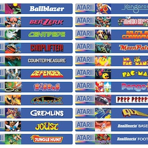 Puede incluir: Una colección de etiquetas de cartuchos de videojuegos Atari de 8 bits. Las etiquetas son azules con texto blanco y gráficos de juegos coloridos. Los títulos incluyen "Ballblazer", "Berzerk", "Centipede", "Choplifter!", "Defender", "Galaxian", "Gremlins", "Joust" y "Jungle Hunt".