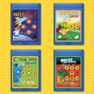 May include: Four blue game cartridges with colorful labels. The labels feature characters and themes from Sesame Street, including Alpha Beam with Ernie, Big Bird's Catch Lab, Cookie Monster Munch, and Oscar's Trash Race.
