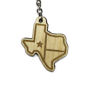 May include: A wooden keychain in the shape of the state of Texas. The keychain features a star and lines etched into the wood, with a silver metal keyring and chain.
