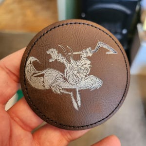以下が含まれることがあります： 帽子をかぶって武器を持った漫画のキツネが白く刻まれた茶色の革製のコースター。キツネは空中でジャンプしている。