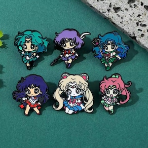 Könnte beinhalten: Set mit sechs Emaille-Anstecknadeln mit Anime-Charakteren. Jede Anstecknadel zeigt einen anderen Charakter mit leuchtenden Haaren und Outfits, mit Details wie Waffen und Accessoires. Die Anstecknadeln sind vor einem türkisfarbenen Hintergrund angeordnet.