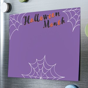 May include: Purple printable Halloween calendar with the text "Halloween Month" in black and orange lettering. The calendar has white spiderwebs in the corners and at the bottom.
