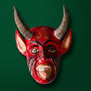 May include: A red devil mask featuring two large, curved, textured brown horns, pointed ears with light centers, wide eyes with yellow irises, black painted eyebrows, and an open mouth revealing white teeth and a tongue, all with a glossy finish.