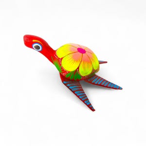 Może przedstawiać: Ręcznie malowana drewniana figurka żółwia. Żółw jest głównie czerwony z żółto-różowym kwiatowym wzorem na skorupie. Nogi mają niebieskie paski, a głowa ma szczegółowe oko.