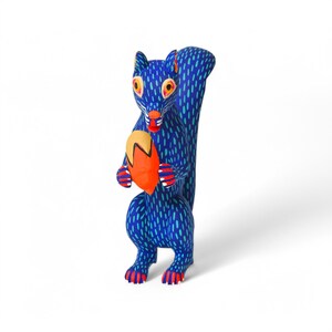 May include: A blue wooden squirrel figurine with orange and yellow accents, holding a red and yellow acorn in its paws.