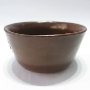 May include: A brown ceramic teacup with a slightly flared rim. The cup has a smooth, matte finish.