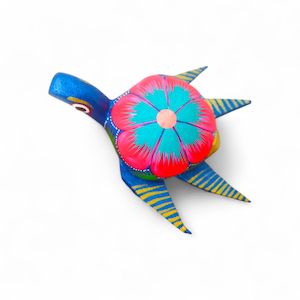 Może przedstawiać: Ręcznie malowana drewniana figurka żółwia. Żółw jest głównie niebieski z dużym kwiatowym wzorem na grzbiecie, z różowymi, turkusowymi i żółtymi akcentami. Nogi mają żółto-niebieskie paski.