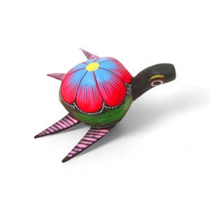 Może przedstawiać: Ręcznie malowana drewniana figurka żółwia z żywym kwiatowym wzorem na skorupie. Skorupa ma kolory czerwony, niebieski i żółty, a głowa i nogi są czarne z różowymi i białymi akcentami. Unikalny element sztuki ludowej.