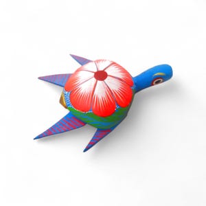 Może przedstawiać: Ręcznie malowana drewniana figurka żółwia. Żółw ma niebieską głowę i płetwy, czerwono-biały kwiatowy wzór na skorupie oraz zielono-niebieski korpus. Figurka jest przedmiotem dekoracyjnym.