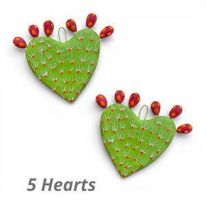 May include: Two heart-shaped cactus ornaments in green, with red and orange details. The cactus ornaments have white spines and a loop for hanging. The text "5 Hearts" is displayed at the bottom.