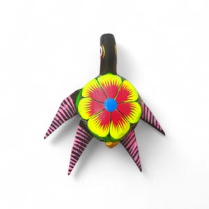 Może przedstawiać: Ręcznie wykonana drewniana figurka ptaka w stylu folk art. Ptak ma czarny korpus, kwiatowy wzór z czerwonymi, żółtymi i niebieskimi akcentami oraz różowe, prążkowane skrzydła. Kolorowy element dekoracyjny.