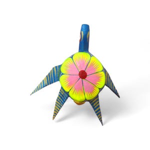 Może przedstawiać: Kolorowa, ręcznie malowana drewniana rzeźba ludowa przedstawiająca stworzenie z ciałem w kształcie kwiatu. Rzeźba ma niebieską głowę i paski na skrzydłach, z dużym różowo-żółtym kwiatem pośrodku. Projekt jest pomalowany jasnymi kolorami.