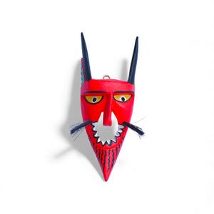 May include: A red devil mask with black horns and yellow eyes. The mask has a jagged mouth and black whiskers. The horns have colorful accents. The mask is made of wood and has a small gold ring at the top for hanging.