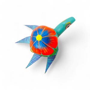 Może przedstawiać: Ręcznie malowana drewniana figurka żółwia. Żółw ma turkusową głowę i nogi oraz skorupę ozdobioną czerwoną kwiatem z niebieskimi płatkami i żółtym środkiem. Nogi mają niebieskie i fioletowe paski.